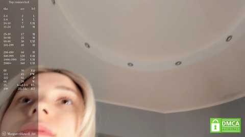 Media: Video of a woman with light skin and long blonde hair, looking upward at a ceiling with recessed lights. A digital overlay displays an HVAC system's specifications.