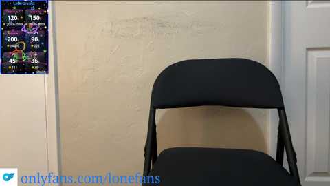 Media: Video of a black folding chair with backrest against a beige wall, featuring a weather forecast screen on the left. Textured wall, closed white door, and a URL watermark at the bottom.