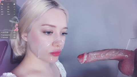 Media: Video of a young, fair-skinned woman with platinum blonde hair, wearing makeup, and covered in semen. Her expression is neutral, and she's in a dimly-lit room with a visible red dildo.