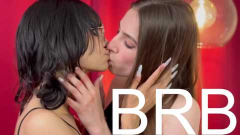 Media: Video of two women kissing passionately; one with short black hair, the other with long brown hair. Background features a red curtain with a modern light fixture. Text \"BBB\" in white.