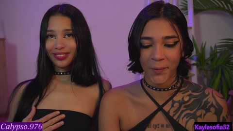 Media: Video of two women with dark hair, one with long hair and a tattoo, the other with a short bob, both wearing black chokers and strapless tops, smiling.