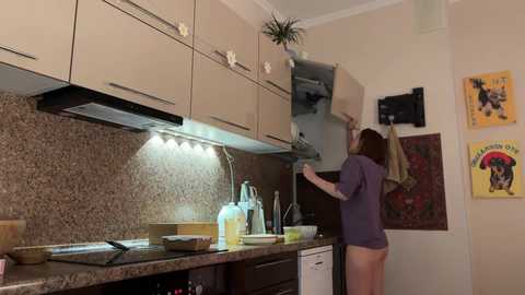 Media: Video of a modern kitchen with a woman in a purple shirt reaching into an open oven, granite countertops, stainless steel appliances, and colorful posters on the wall.