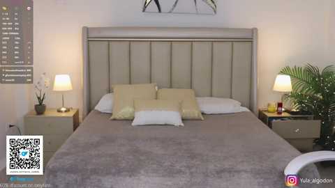 Video of a modern, minimalist bedroom with a beige tufted headboard, two bedside lamps, a potted plant, and a QR code.