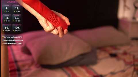 Video of a close-up of a hand wearing a red bandage on a bed with pink and red plaid sheets, blurred background.