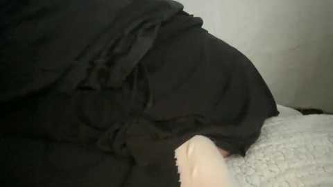 Media: A video showing a close-up of a person lying on a white, plush blanket, covered with black clothing, with a pale hand visible, suggesting a sleeping or resting state.