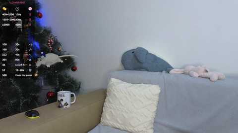 A video shows a cozy living room with a decorated Christmas tree, plush toys, and a soft gray blanket on a couch.