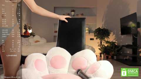 Media: Video of a woman in a plush, bunny costume with a black chair, in a modern, warmly lit living room with plants and a TV.