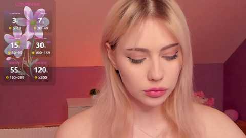 Media: Video of a young blonde woman with fair skin and minimal makeup, wearing a strapless top, in a pink-lit bedroom with a digital flower clock and a pink bedspread.