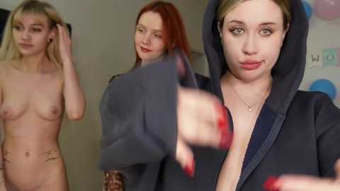 Media: Video of three women in a room: one nude with small breasts, one in a grey hoodie, and one in a black hoodie.