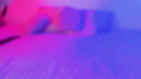 This is a blurred, abstract image featuring a mix of pink, purple, and blue colors. The image has a soft, hazy texture, making it difficult to discern specific objects or details.