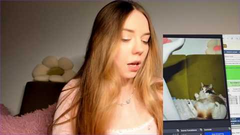 Media: Video of a Caucasian woman with long, straight, light brown hair, wearing a pink top, watching a laptop screen showing a cat. Background includes a plush toy and a green wall.