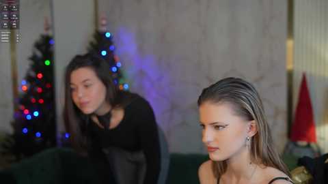 Media: Video of two young women, one with long brown hair, the other with wet, slicked-back blonde hair, in a festive indoor setting with Christmas lights and a decorated tree in the background.