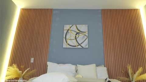 Video of a modern bedroom with a blue wall, orange wood-paneled headboard, white bedding, and abstract art above the bed.