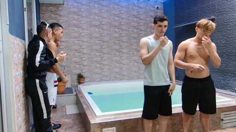 Video of four shirtless men in a small, modern, outdoor hot tub area; one is seated, two are standing, and one is approaching.