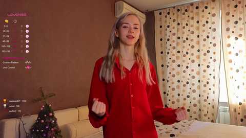 Media: Video of a blonde woman in a red shirt, dancing in a cozy bedroom with a Christmas tree and polka-dotted curtains.