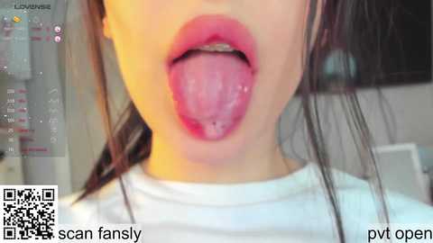 Video of an Asian woman's face, partially obscured by her outstretched tongue, wearing a white shirt. Background shows a calendar and a QR code.