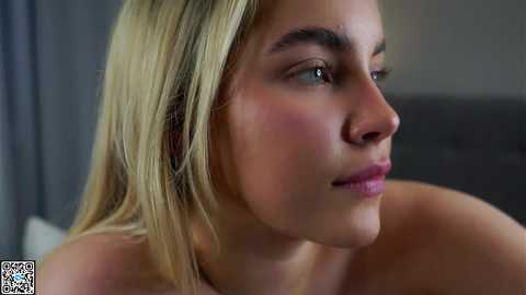 Video of a close-up side profile of a young woman with fair skin, straight blonde hair, and light makeup. She has a serene expression, with her gaze slightly upward.