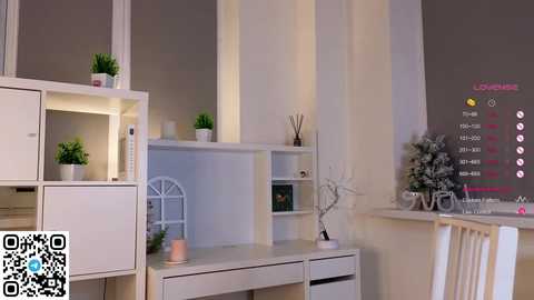 Media: Video of a minimalist, white-walled living room with sleek white furniture, potted plants, and a modern LED TV displaying a digital clock and weather forecast.