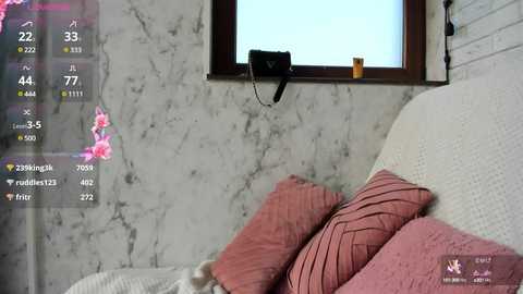 Video of a cozy bedroom with a white, textured headboard adorned with pink, ruffled pillows. The background features a marble-patterned wall and a small window. A digital clock and weather display overlay the scene.