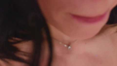 Close-up video of a woman's face, focusing on her lips painted in vibrant pink lipstick. She has a delicate silver necklace with a small pendant. Her dark hair is visible in the background.