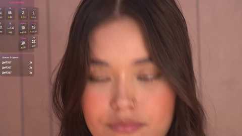 Video of a young Asian woman with long, wavy black hair, closed eyes, and a serene expression. Background features a digital calendar displaying dates and appointments.