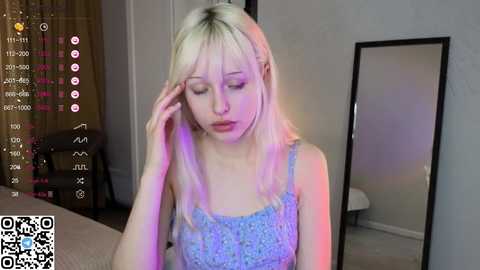 Media: Video of a pale, slender, blonde woman in a blue floral dress, appearing exhausted, with a mirror and dimly lit room in the background.