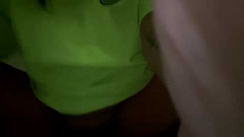 A blurry, dimly lit video shows a person in a green T-shirt and dark pants, standing with a hand on their hip. The background is dark and indistinct.