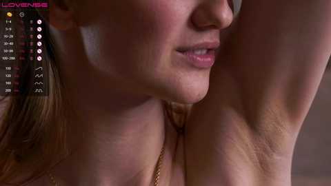 Close-up video of a woman's upper body, showing her armpit and shoulder. She has fair skin and light brown hair, and her mouth is partially open. The background is blurred, with a digital display showing temperature and heart rate on the left.