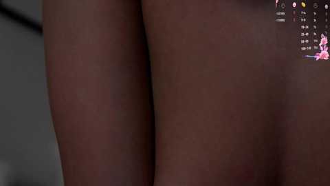 Video of a close-up of a person's bare buttocks, with a dark skin tone, viewed from the side. The background is blurred, and a digital screen with a pink and purple interface is visible in the top right corner.