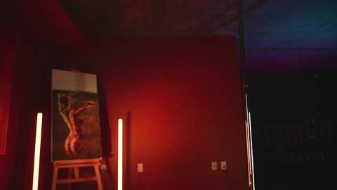 Video of a dimly lit, red-walled room with a wooden chair, a standing lamp, and a dark, abstract painting on the wall, with blue and purple lights in the background.