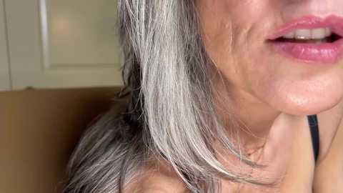 Video of a close-up of an older woman with light gray hair, wearing a black spaghetti-strap top, her face partially visible, lips slightly parted.