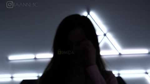 Media: A dimly lit video of a woman with long, dark hair, partially obscured by a glowing, geometric light pattern in the background, likely in an urban setting.