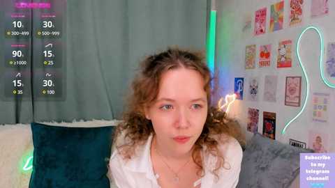 A video of a young woman with curly brown hair and a white top, seated on a teal couch, surrounded by colorful posters and neon lights, with a digital overlay displaying social media stats.