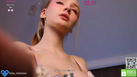 Video of a young woman with light skin and blonde hair, wearing a pink bra, captured in a dimly lit room with a time stamp \"22:01\" in the top right corner.