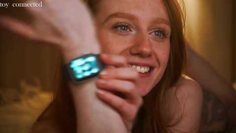 Media: Video of a young, smiling woman with red hair, wearing a black smartwatch, in a dimly lit room.