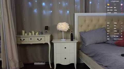 Video of a cozy, modern bedroom with beige walls, a tufted headboard bed, white bedside table, and a fluffy white lampshade.