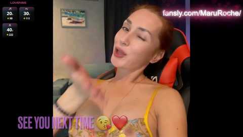 Media: Video of a fair-skinned woman with red hair, wearing a yellow lace bra, sitting on a red gaming chair, with a blurred background, overlaying a \"See You Next Time\" text.