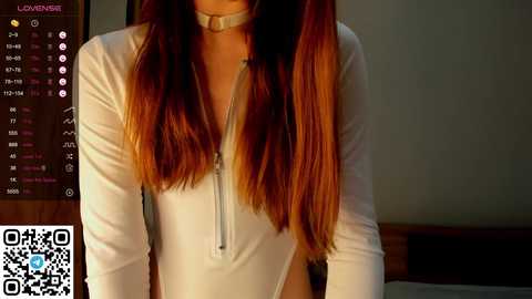 Media: A video shows a woman with long, straight, auburn hair in a white, long-sleeved, zip-up bodysuit with a choker. The background features a wooden headboard and a digital clock with a QR code.