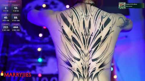 Media: Video of a tattooed back featuring a detailed, abstract black and white design resembling a feather pattern. The background is dimly lit with purple and blue hues, and the image includes a \"Marry Me\" overlay.