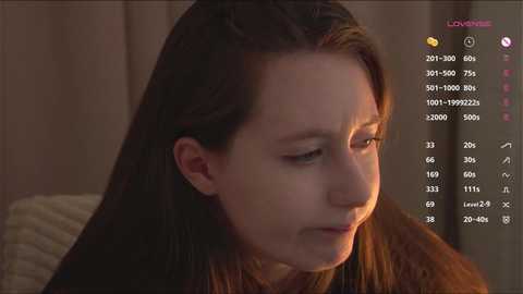 Video of a young woman with straight, brown hair, wearing a brown sweater, looking sad. Background shows a beige wall and a pink text overlay with social media metrics.