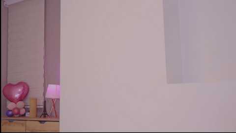 Video of a minimalist, cream-colored wall with a heart-shaped pink balloon on a wooden shelf in the background.