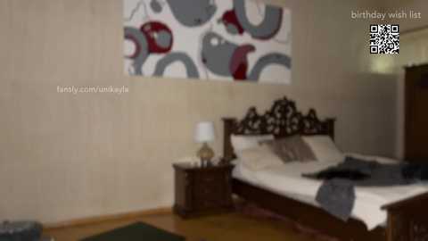 Media: A dimly lit bedroom photo with a bed, wooden nightstand, white lamp, and abstract art on beige walls. Text reads \"birthday wish list.\