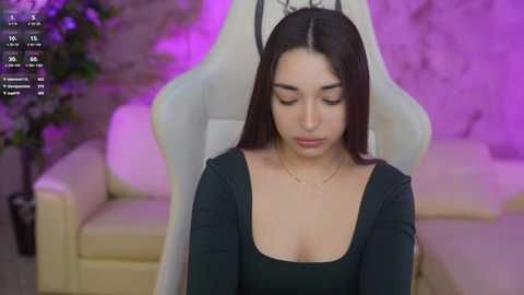 Media: A video of a young woman with long dark hair, wearing a black top, sitting on a white gaming chair in a dimly lit room with purple lighting.