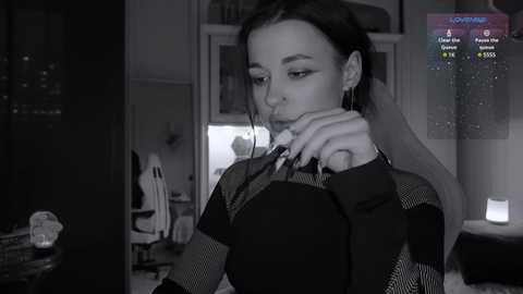 Media: Black-and-white video of a young woman with dark hair, wearing a checkered shirt, looking at a computer screen in a dimly lit room.