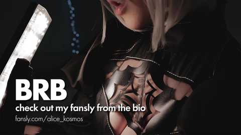 Video of a woman with light skin and short, blonde hair, wearing a black, cut-out top revealing her chest. She holds a flashlight in her gloved hand. Text reads \"BRB out my fanly from the bio.\