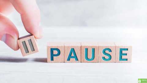 Media: A video shows a hand holding a wooden block with \"PAUSE\" in blue letters, placed on a light-colored wooden floor. The background is blurred, emphasizing the tactile wooden textures and simplicity.