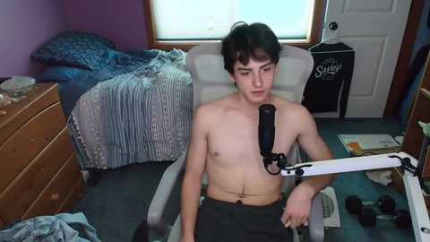 Media: Video of a young, shirtless boy with short dark hair wearing a black brace on his right arm, sitting on a chair in a messy bedroom.