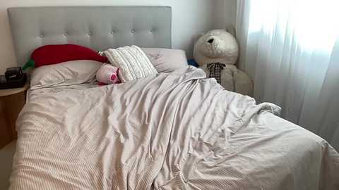 Media: A video of a tidy, modern bedroom with a beige tufted headboard, white bedding, a plush white teddy bear, and a red pillow.