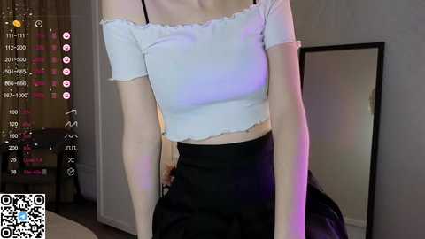 Media: Video of a slender, fair-skinned woman in a white off-shoulder crop top and black high-waisted skirt, posing indoors with a QR code overlay.