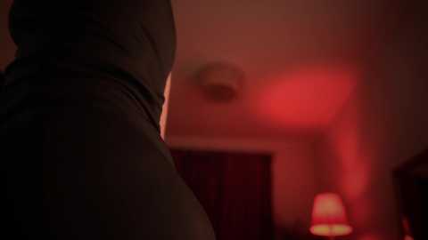 Media: A dimly lit video shows the lower half of a person in a dark outfit, possibly wearing a jacket, standing in a room with red lighting, creating a moody atmosphere.